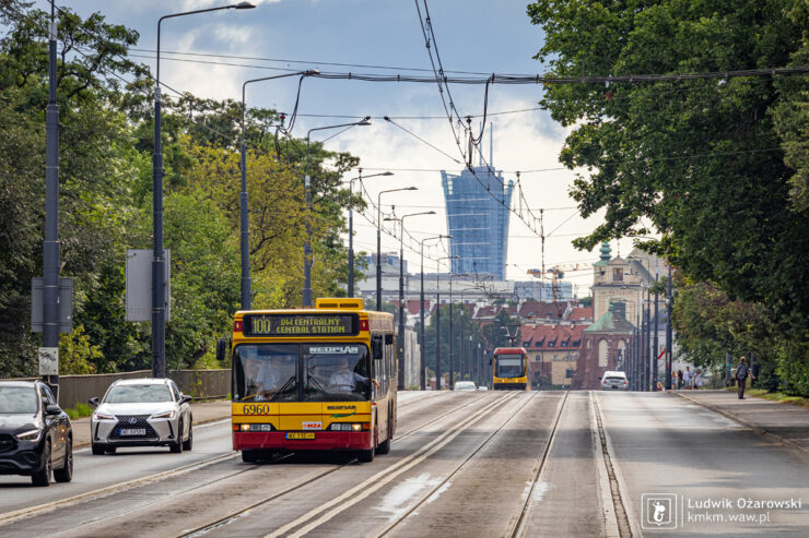 Piętnastometrowy Neoplan na Trasie W-Z z zabytkową zabudową i wieżowcem Warsaw Spire w tle
